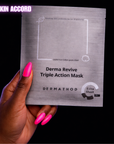 Hand holding a Dermathod Derma Revive Triple Action Mask against a black background