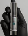 Hand wearing a black glove holding a silver and gray serum bottle labeled 'neo genesis' against a gray background.