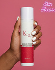 Hand holding a Krx Aesthetics anti-acne toner bottle against a pink background