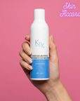 Hand holding a bottle of KRX Probiotic Face Wash against a pink background
