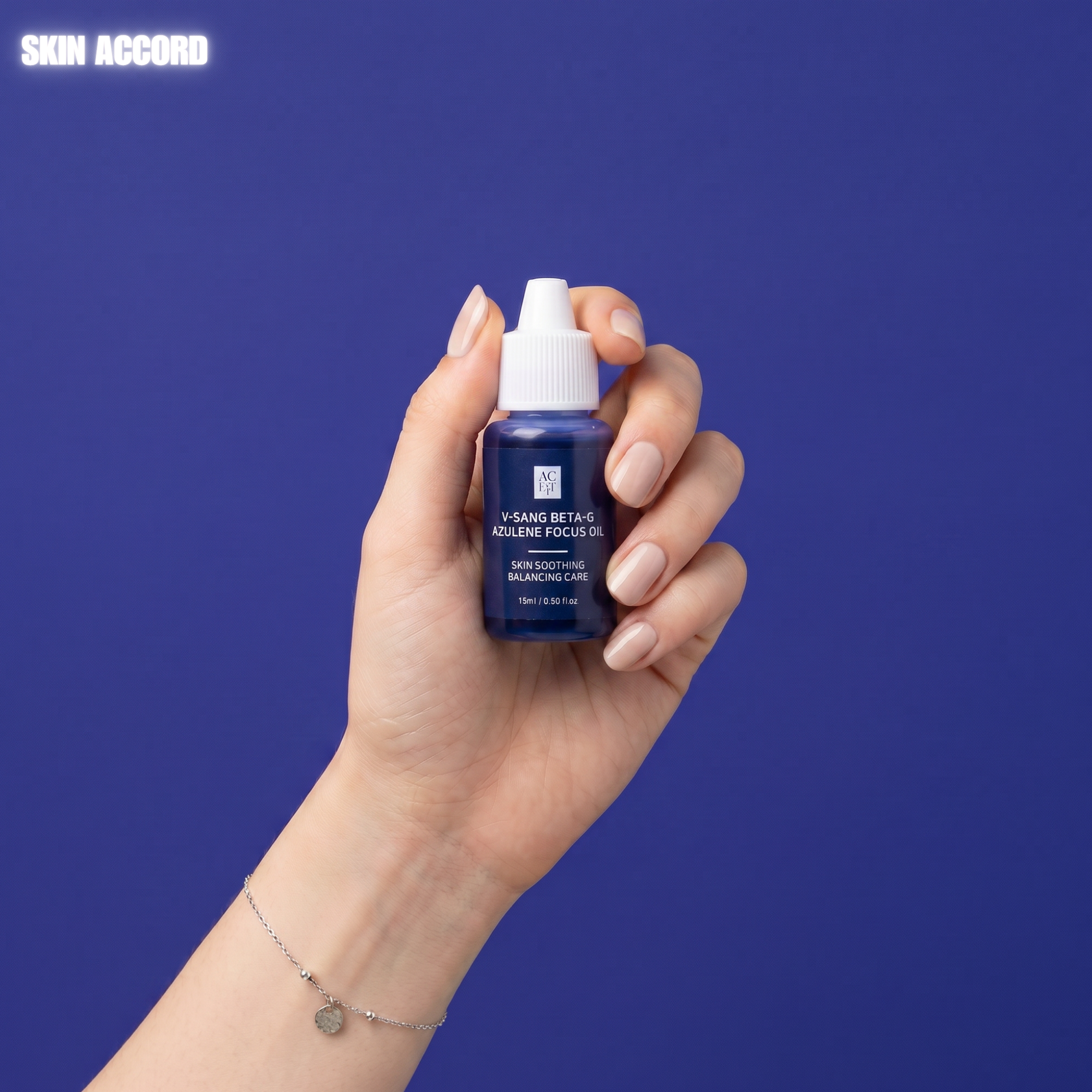 A hand with manicured nails holds  bottle of AC Fit V Sang Azulene Focus Oil against a solid blue background.
