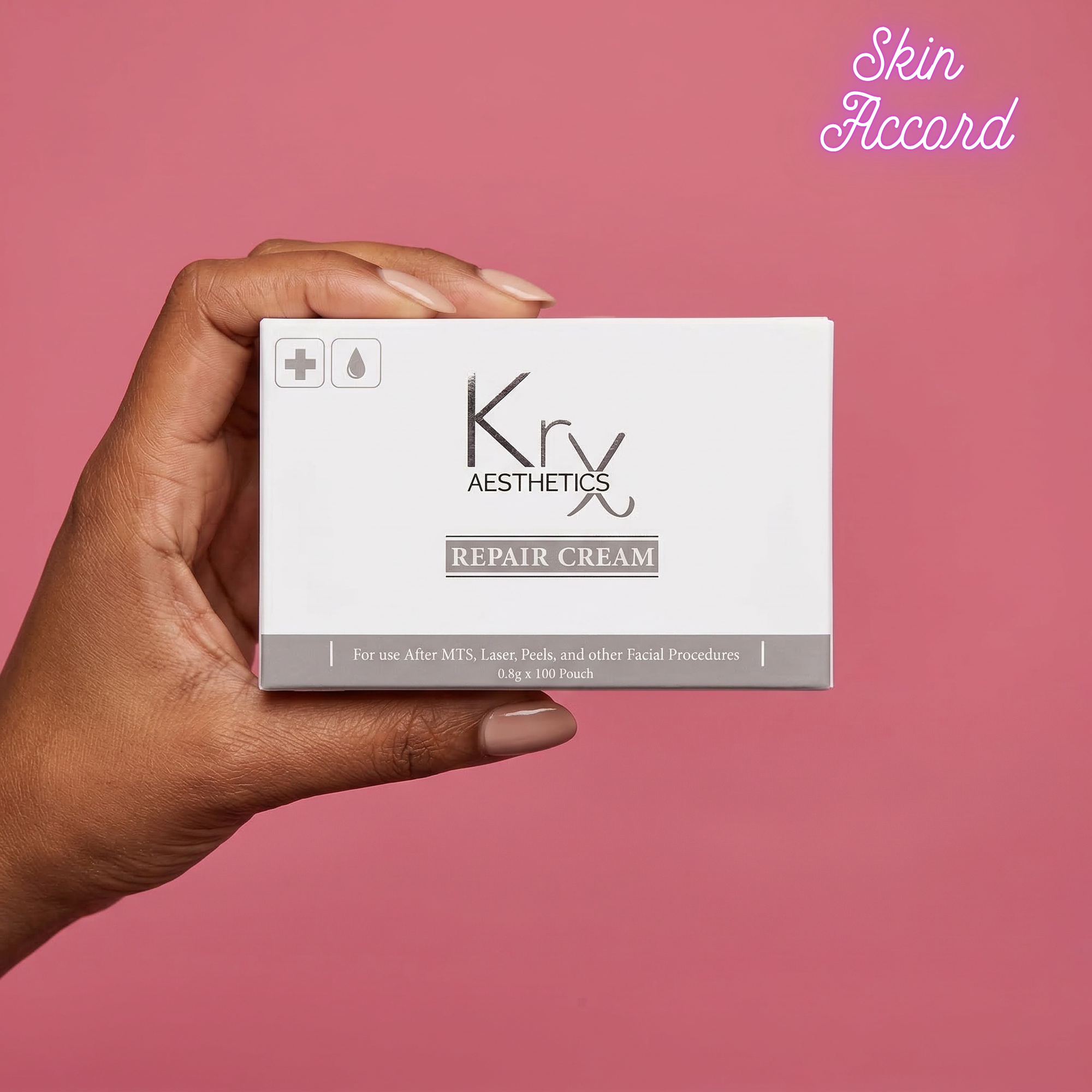 Hand holding a box of Krx Aesthetics Repair Cream against a pink background
